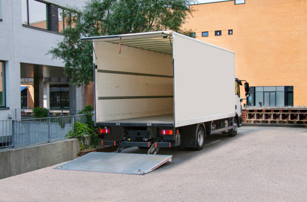 Camion de livraison blanc vide avec hayon ouvert devant un immeuble de bureaux.